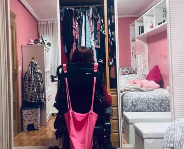 Una mujer en silla de ruedas mira su armario abierto.